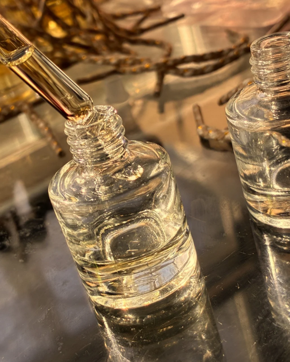 Clear glass bottle with dropper on a reflective surface, with 'Afriquearomas' branding.