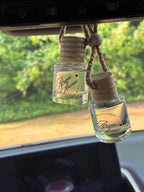 Two small glass bottles with wooden caps hanging from a car's rearview mirror.